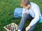 Cute young boy in blue shirt plays chess on grass in park, outdoor. Hobby, education