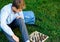 Cute young boy in blue shirt plays chess on grass in park, outdoor. Hobby, education,