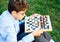 Cute young boy in blue shirt plays chess in the summer park . Hobby, education,