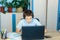 Cute young boy in blue shirt sitting behind desk in his room next to laptop and study. Teenager in earphones makes homework,