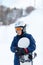 Cute young boy in gray helmet and orange googles, in blue jacket holds snowboard on white snow background. winter sport