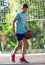 A cute young boy plays basketball on the street playground in summer. Teenager in a green t-shirt with orange basketball ball