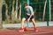 A cute young boy plays basketball on the street playground in summer. Teenager in a green t-shirt with orange basketball ball