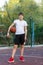 Cute young boy plays basketball on street playground in summer. Teenager in white t-shirt with orange basketball ball outside.