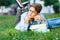 Cute, young boy in round glasses and blue shirt writes with his left hand while lying on the grass in the park. Education,