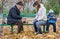 Cute young boy sitting on a park bench holding a tablet computer while his mother and grandfather play chess