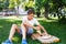 Cute, young boy in white t shirt sits on the grass and takes a slice of pizza in the summer park. Boy eats pizza