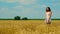 Cute young brunette woman with beautiful long hair in white short summer sundress stands on golden wheat field