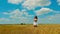 Cute young brunette woman with beautiful long hair and white short summer sundress walks on golden wheat field