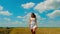 Cute young brunette woman with beautiful long hair and white short summer sundress walks on golden wheat field