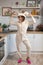 Cute young brunette woman in fluffy pajamas on a white scandinavian kitchen