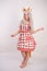 Cute young caucasian girl in kitchen plaid apron with fluffy Fox ears and long fur red tail standing barefoot on white background