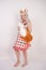 Cute young caucasian girl in kitchen plaid apron with fluffy Fox ears and long fur red tail standing barefoot on white background