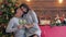 Cute young couple with wineglasses sits on background of fir tree on eve of new year