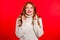 Cute young girl with beautiful hairstyle praying over red background. Woman begging someone.