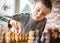 Cute young happy boy chess genius concentrating playing game of strategy moving piece sitting at wooden table chessboard happy