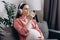 Cute young pregnant woman listening to music in wireless headphones, enjoy pure fresh cool mineral water at morning. Future mother