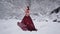 Cute young woman in fairy tale image in red royal dress with white violin stands on snow in winter forest