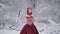 Cute young woman in fairy tale image in red royal dress with white violin stands on snow in winter forest