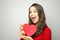 Cute young woman holding a paper heart wink and smile at camera on gray background. Valentine`s Day concept