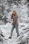 A cute young woman with long blond hair in a knitted cozy cardigan walks through the winter snowbound forest