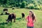 Cute young woman with long hair and braces hiking through green meadow with cows