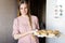 Cute young woman in a pink dress with a scythe in the kitchen near the refrigerator. the mistress in her kitchen. a housewife.