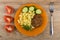 Cutlet with pasta, cucumbers in plate, pieces of tomato, fork