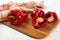 Cutting board with several whole and halves of red bell pepper and red kitchen towel on white wooden background