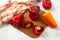 Cutting board with several whole and halves of red and yellow bell pepper and red kitchen towel on white wooden background