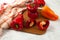 Cutting board with several whole and halves of red and yellow bell pepper and red kitchen towel on white wooden background