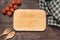 Cutting board with tomato, fork and spoon on wooden background