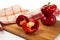 Cutting board with whole and half of red bell pepper and red kitchen towel on white wooden background