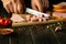 Cutting parboiled sausage on wooden cutting board at domestic kitchen by hands cook for a sandwich. Space on black background for