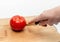 Cutting red tomato with knife into two halves on wooden kitchen board. Woman\'s hand cuts a tomato