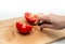 Cutting red tomato with knife into two halves on wooden kitchen board. Woman\'s hand cuts a tomato