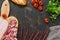 Cutting various sausages with tomatoes, baguette on a dark background, space for text. View from above.