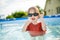 Cuty funny toddler boy having fun in outdoor pool. Child learning to swim. Kid having fun with water toys. Summer activities for