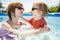 Cuty funny toddler boy and his teenage sister having fun in outdoor pool. Child learning to swim. Kid having fun with water toys.