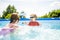 Cuty funny toddler boy and his teenage sister having fun in outdoor pool. Child learning to swim. Kid having fun with water toys.