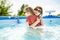 Cuty funny toddler boy and his teenage sister having fun in outdoor pool. Child learning to swim. Kid having fun with water toys.