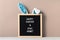 Cyan bunny ears and black felt letter board with a slogan - Happy Easter and Stay at Home on a beige background