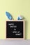 Cyan bunny ears and black felt letter board with a slogan - Happy Easter and Stay at Home on pastel green background