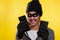 Cybercrime and money theft. A woman in a hat and mask with a malicious smile, holding phones. Yellow background. Copy space