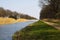 Cycling tour along straight canal with reed and bare trees on the riverbank in spring