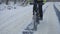 Cycling in the winter through a snowy forest. The cyclist rides on a slippery asphalt road. Male feet are pedaling. A