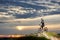 Cyclist with bicycle rests on cliff top in mountains enjoying sun at sunset under an unusual sky