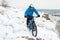 Cyclist in Blue Riding Mountain Bike on Rocky Winter Hill Covered with Snow. Extreme Sport and Enduro Biking Concept.