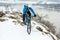 Cyclist in Blue Riding Mountain Bike on Rocky Winter Hill Covered with Snow. Extreme Sport and Enduro Biking Concept.