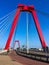 Cyclist crossing the Willemsbrug bridge spanning the Nieuwe Maas river in Rotterdam, the Netherlands. Red bridge pylons and cables